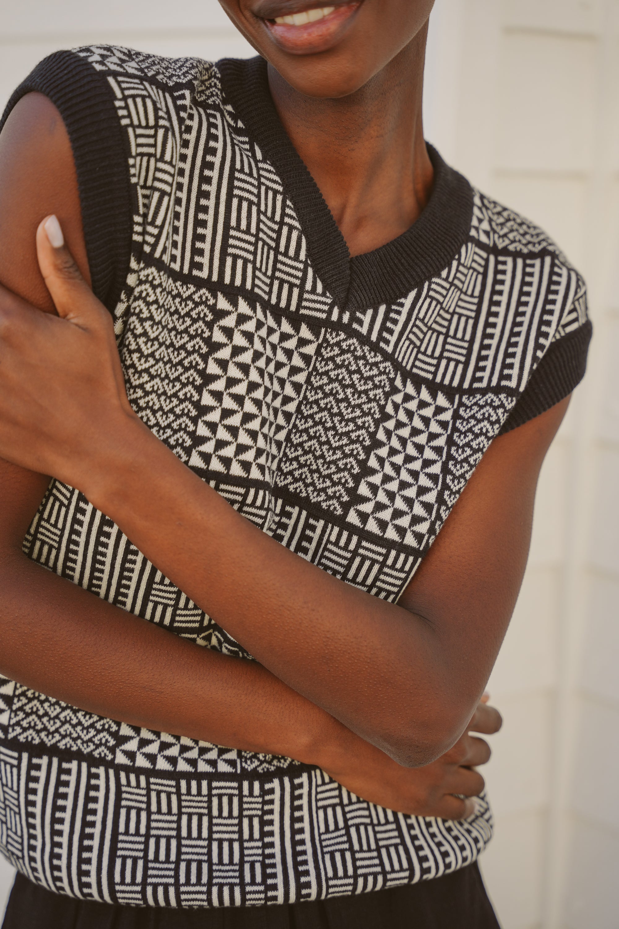Model, Zana, wearing the sleeveless black & ecru Ade Vest with Zuri pattern against a neutral background.
